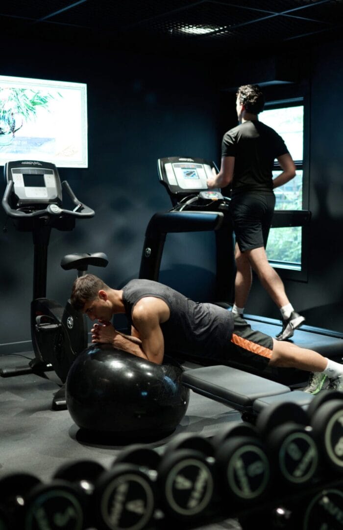 Men working out in a modern hotel gym with treadmill, exercise bike, and weights at Abstract Hotel.