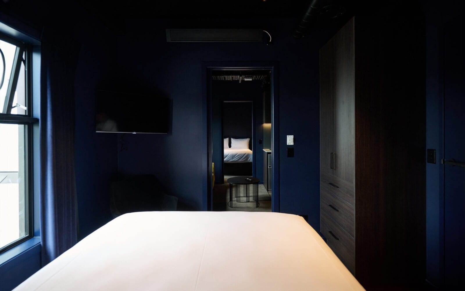 Modern hotel suite with deep blue tones, two beds, and a cozy lounge area.