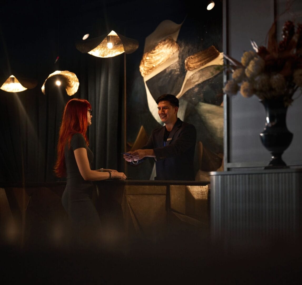 Hotel guest checking in at a warmly lit reception desk with modern lighting and abstract wall art in the background.